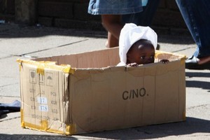 A mother and her daughter walk past a baby playing in a box in Harare. There are signs of looming elections. Photo / AP