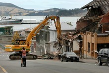 Diggers demolish a damaged building in Lyttleton as residents console one another. Photo / Brett Phibbs