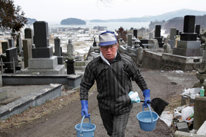 Takayuki Sato carries buckets of water to clean the family grave in Minamisanriku, nearly a year after the March 11 tsunami hit his home town. Photo / AP