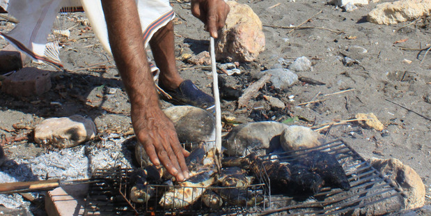 A fisherman cooks lunch on the beach in the Omani port town of Quriyat. Photo / Jim Eagles