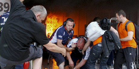Williams's team mechanics help an injured colleague as they escape the team garage destroyed by fire. Photo / AP