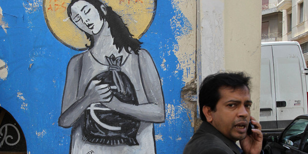 An man talks on his mobile phone in front of graffiti depicting an angel with a bag of euros, in Athens. Recent polls suggest rising support for the country's international rescue package. Photo / AP