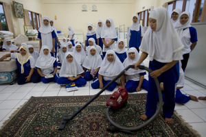 Women learn to vacuum in Jakarta in 2006 at a training centre that sends domestic workers abroad. Above right, the Auckland Ferry Building, by Henry Winkelmann in 1913. Photo / Magnum, Auckland Libraries