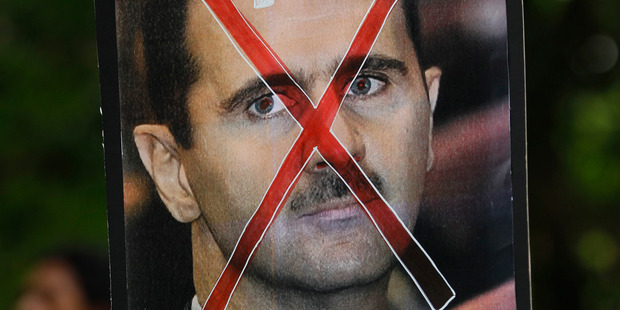 A protester holds up a poster of Syrian President Bashar al-Assad with cross mark over it during a protest rally against Assad's regime outside. Photo / AP