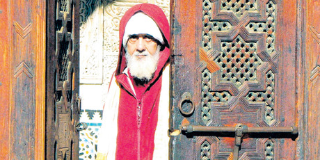 A man in a red jellaba stares out from an intricately carved doorway in Fez. Photo / Guy Needham