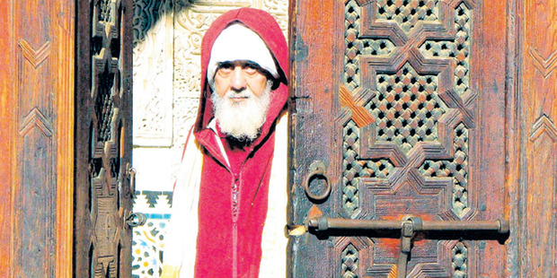 A man in a red jellaba stares out from an intricately carved doorway in Fez. Photo / Guy Needham