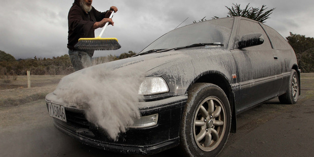 Vic Cassin sweeps ash from one of the vehicles parked on his section near Turangi, which was in the path of the ash cloud that resulted from last nights eruption of Mt Tongariro. Photo / Alan Gibson
