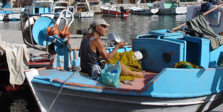 Fisherman mend nets from their blue and white wooden caiques in Symi's harbour. Photo / Lois Green