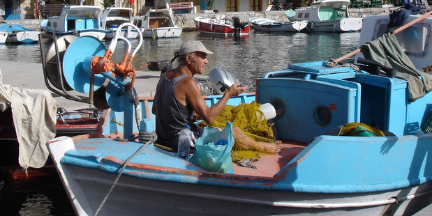 Fisherman mend nets from their blue and white wooden caiques in Symi's harbour. Photo / Lois Green