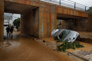 Residents walk by a wrecked car carried away by flash floods after heavy rain in the town of Villanueva del Rosario, Malaga, southern Spain. Photo / AP