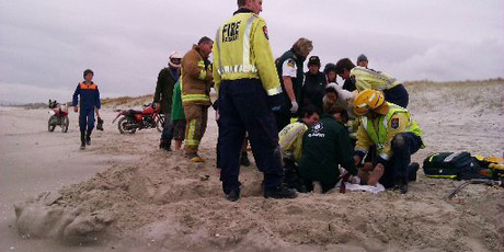 The injured teenager being attended to by St John paramedics inside a sand wall that volunteer firefighters erected at Ruakaka Beach. Photo / Mark Going