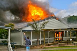 A bystander uses a garden hose to dampen down a nearby classroom block before the fire service arrives. Photo / Lesley Staniland