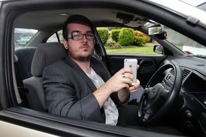 Sam Murdie with his car and iPhone. He is angry at being fined for taking a photograph of a crash scene. Photo / Doug Sherring