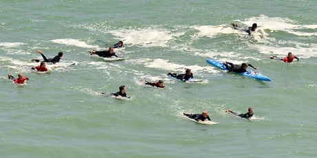 Dave Rastovich is escorted into Piha Beach by local surfers and supporters. Photo / Paul Hogan