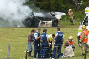 Kerikeri firefighters douse the crashed car while rescuer Mary Elliott (obscured) and emergency personnel comfort the children pulled from the wreckage. Photo / Supplied