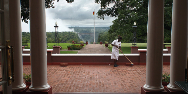 Spray from Victoria Falls shoots into the air in the distance as a maid cleans the terrace of the historic Victoria Falls Hotel. Photo / Getty Images