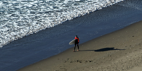 A surfer walks along Ngarunui (Ocean) Beach in Raglan as the sun sinks low on the horizon. Photo / Alan Gibson