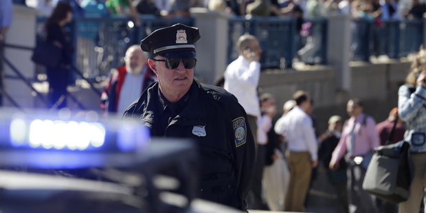 A Boston police officer stands guard as people stand on a bridge outside the John Joseph Moakley Federal Courthouse. Photo / AP