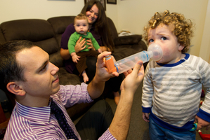 Two-year-old Berkeley Ballinger-Judd is helped by his father, Rob, to take his asthma medicine as mum Jenner and younger brother Clarke watch. Photo / Richard Robinson