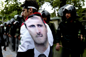 An Syrian man wrapped in a Syrian flag with a portrait of President Bashar Assad, walks past anti riot police during an anti-Israeli demonstration in Iran. Photo / AP