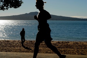 A walker and jogger enjoy the early morning winter sun, Cheltenham Beach, Devonport. Photo / Michael Craig
