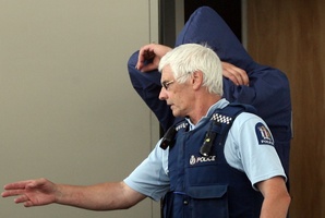 A police officer leads one of the accused into court during an earlier appearance. Photo / Wairarapa Times-Age