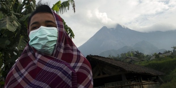 A resident of Cangkringan district in Indonesia's Central Java province wears mask to protect himself against volcanic ash from Mount Merapi (background) after spewing volcanic ash.Photo / AFP