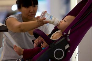 A woman feeds milk to her baby on a stroller at a shopping mall in Beijing. Photo / AP