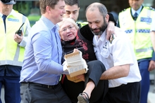 A woman with a cardboard splint is carried to a police car at the railway station. Photo / SNPA
