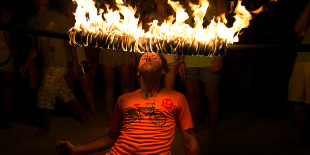 A man attempts to light a cigarette while walking underneath a burning rod during a limbo dance at the full moon party on the beach. Photo / Getty Images