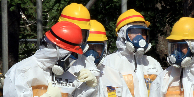 Japanese Prime Minister Shinzo Abe, left, tries to peel off his name pasted on a protective suit after finding a wrong character used for his family name. Photo / AFP