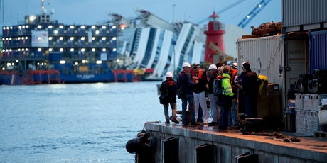 Workers gather before the operation to refloat the Costa Concordia, seen in the background. Photo / AP