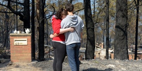 Amy Hubbard and her partner Adam Ilhan stand in front of the burnt out ruins of her parents' home which was destroyed by bushfires in Winmalee in Sydney's Blue Mountains. Photo / AFP