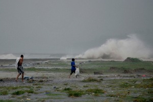 Residents sift through the shoreline amidst a storm surge brought about by powerful typhoon south of Manila.Photo / AP