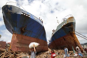 Survivors pass by two large boats after they were washed ashore by strong waves caused by Typhoon Haiyan in Tacloban city. Photo / AP
