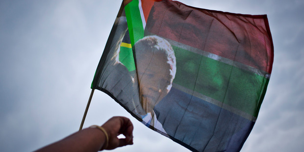 Mourners hold aloft a Nelson Mandela flag as they sing and dance to celebrate his life. Photo / AP