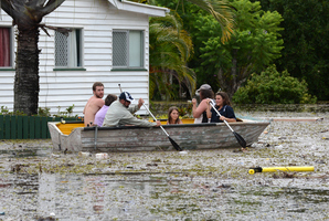 People in a boat negotiate flood water and debris in Bundaberg, Queensland. Photo / AAP