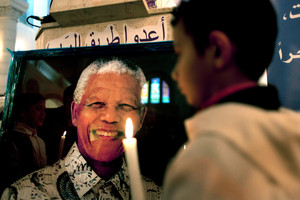 A Palestinian child holds a lit candle as he prays in front of a poster of late South African leader Nelson Mandela, during a special service in his honour in the West Bank. Photo / AP