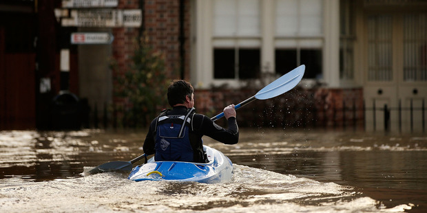 A man canoes along the town centre streets submerged under floodwater checking on people in Yalding, England. Photo / Getty Images