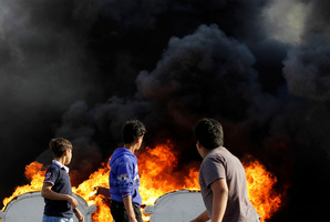 Bahraini boys look at an anti-government protester, unseen, as he adds fuel to old furniture being set on fire in a street in Malkiya, Bahrain. Photo / AP