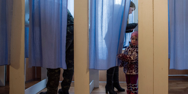 A young girl peeks out of a voting booth at a polling station during the Crimean referendum, in Orlinoe, near Sevastopol, Ukraine. Photo / AP