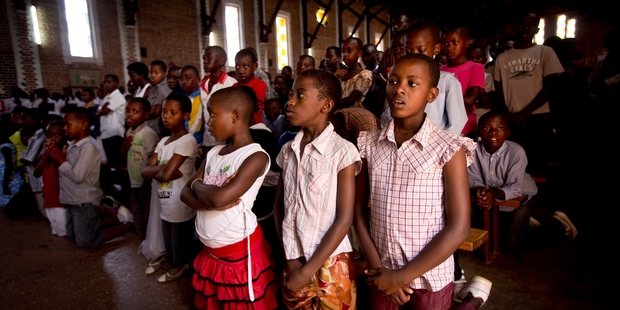 Rwandan children, not alive at the time of mass killings, pray for the victims in a Kigali church where many were murdered. Photo / AP
