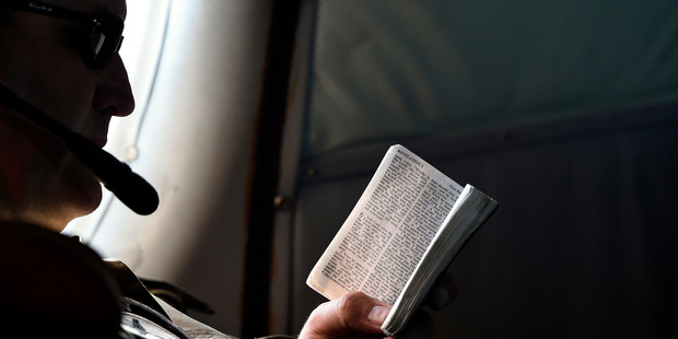 Flight Engineer Chris Poole reads a small bible aboard a Royal New Zealand Air Force (RNZAF) P-3 Orion on route to search over the southern Indian Ocean. Photo / AP