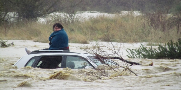 A woman, left, waits to be rescued from her car roof after the flooded Kakanui River washed it off the road. Photo / Otago Daily Times