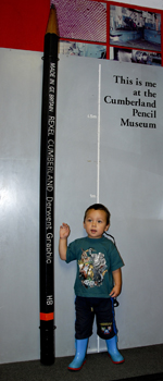 A child stands next to a<BR>very tall pencil at the<BR>museum in Keswick.