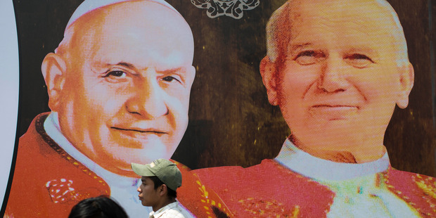 Two people walk in front of pictures of Pope John XXIII, left, and Pope John Paul II in Guatemala City. Photo / AP