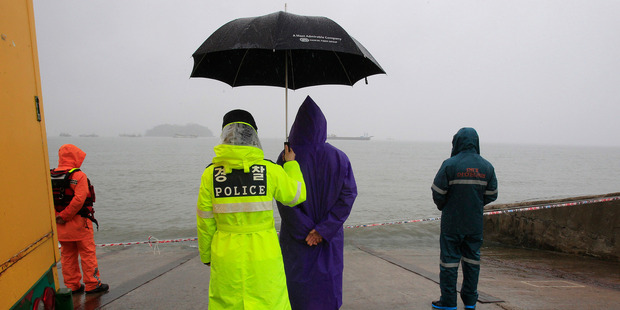 A police officer holds up an umbrella for a relative of a passenger aboard the sunken ferry Sewol. Photo / AP