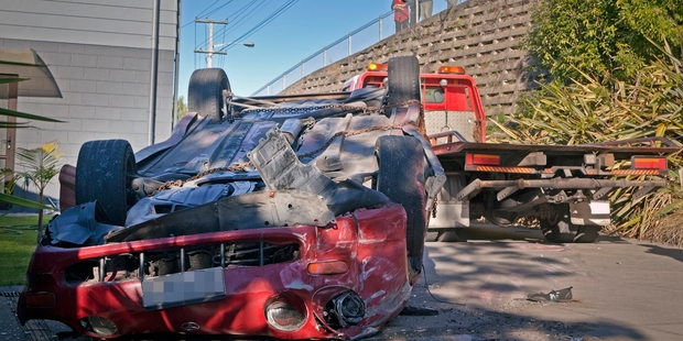 The driver suffered a broken leg when her car landed on its roof, after going through the fence and flying over another vehicle parked in the driveway. Photo / APN