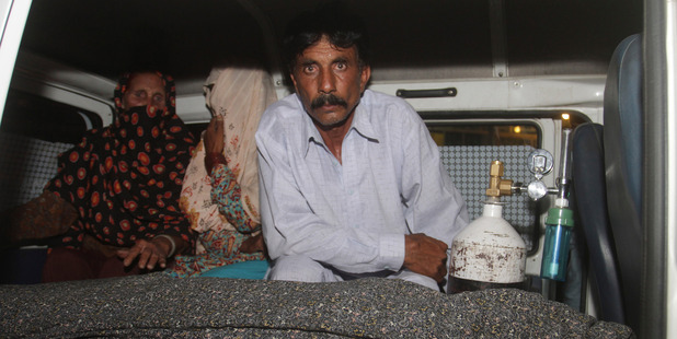 Mohammad Iqbal, right, husband of Farzana Parveen, sits in an ambulance next to the body of his pregnant wife. Photo / AP