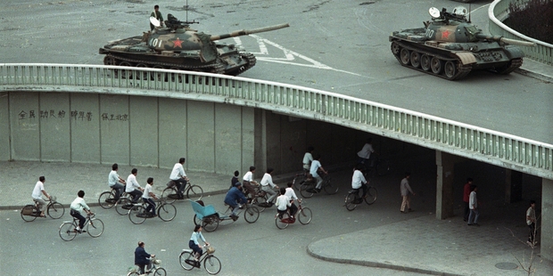 Bicycle commuters pass through a tunnel while, above, tanks are positioned in Beijing, two days after the Tiananmen Square killings. Photo / AP